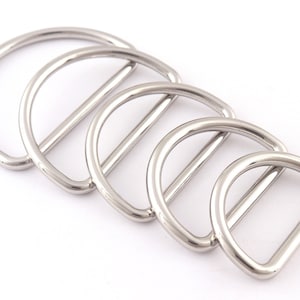 May include: Four silver metal D-rings of different sizes. The rings are arranged in a row, with the largest ring on the left and the smallest ring on the right.