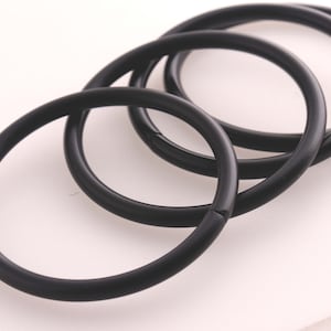 Puede incluir: Cuatro anillos de metal negro de diferentes tamaños, apilados uno encima del otro.