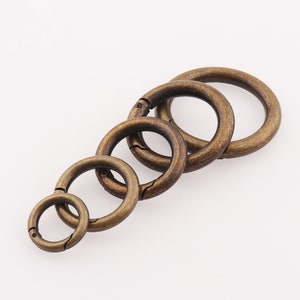 Puede incluir: Conjunto de cinco llaveros de metal de color dorado antiguo con cierre de resorte. Los anillos están anidados entre sí en orden decreciente de tamaño.