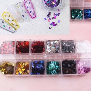 Può includere: Un contenitore di plastica trasparente con 12 scomparti pieni di glitter a forma di farfalla di vari colori. Il glitter è in tonalità di rosso, oro, blu, verde, nero e bianco.