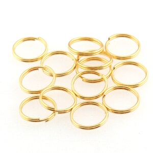 Puede incluir: Un grupo de 12 anillos de salto de color dorado. Los anillos son todos del mismo tamaño y están dispuestos en una pila suelta.