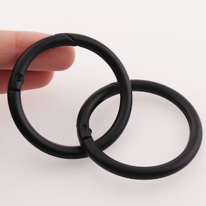 Könnte beinhalten: Zwei schwarze Schlüsselringe aus Metall mit einem Drehverschluss. Die Ringe sind ineinander verschlungen.