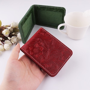 May include: Two leather wallets, one green and one red. The red wallet has a floral pattern and a white stitch around the edges. The green wallet has a white stitch around the edges.