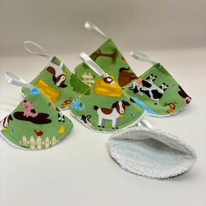 May include: Five green fabric ornaments with farm animal patterns, each with a white ribbon loop. The ornaments feature images of pigs, cows, goats, and other farm animals. The reverse side of the ornaments is white.