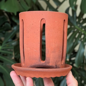 May include: Terracotta pot with drainage holes and a matching saucer. The pot has a rustic, earthy look and is perfect for small plants.