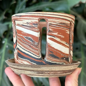 以下が含まれることがあります： 大理石模様の茶色と白のセラミック製のプランター。排水穴と受け皿付き