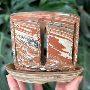 以下が含まれることがあります： 大理石模様のテラコッタ色のセラミックプランター。排水穴と、それに合う受け皿が付いています。