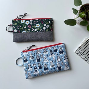 May include: Two zippered pouches, one with a floral print in shades of green and white, and the other with a blue background and a repeating pattern of pirates and treasure chests.