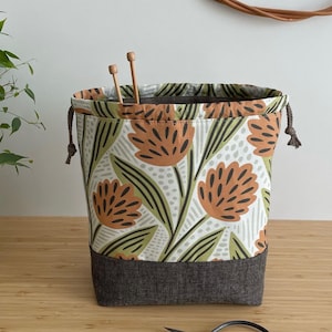 Pode incluir: Uma bolsa de cord&atilde;o com estampa floral em tons de verde, marrom e branco. A bolsa tem um fundo cinza escuro e &eacute; feita de tecido.