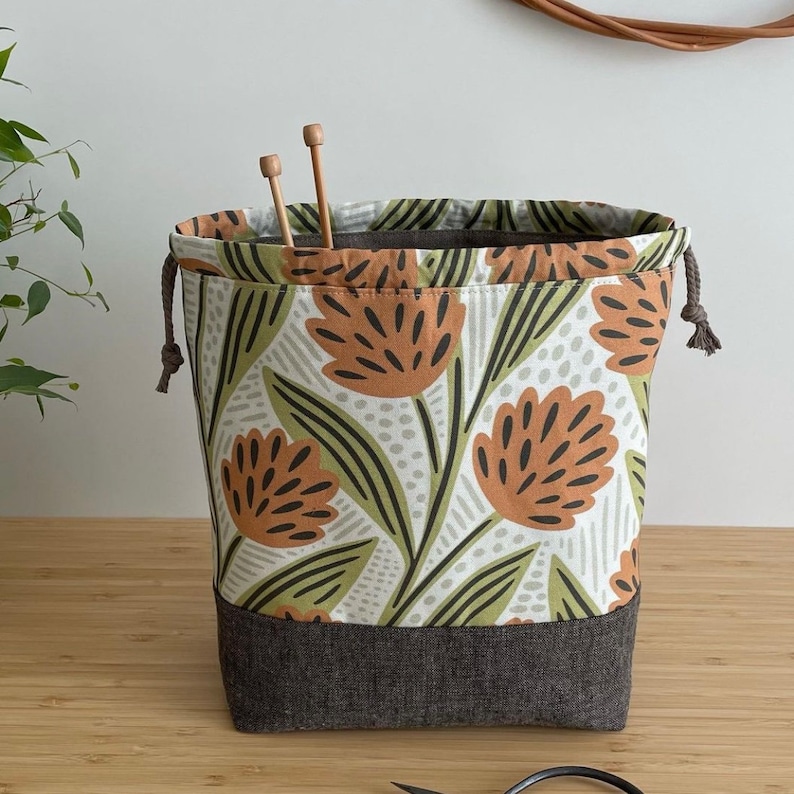 Pode incluir: Uma bolsa de cord&atilde;o com estampa floral em tons de verde, marrom e branco. A bolsa tem um fundo cinza escuro e &eacute; feita de tecido.