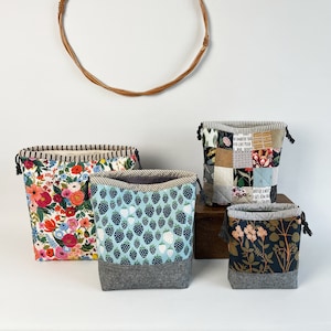 Pode incluir: Quatro sacos de cord&atilde;o com padr&otilde;es diferentes. Os sacos s&atilde;o feitos de tecido e t&ecirc;m um cord&atilde;o cinzento. Os padr&otilde;es incluem flores, morangos, um design de patchwork e um design floral escuro.