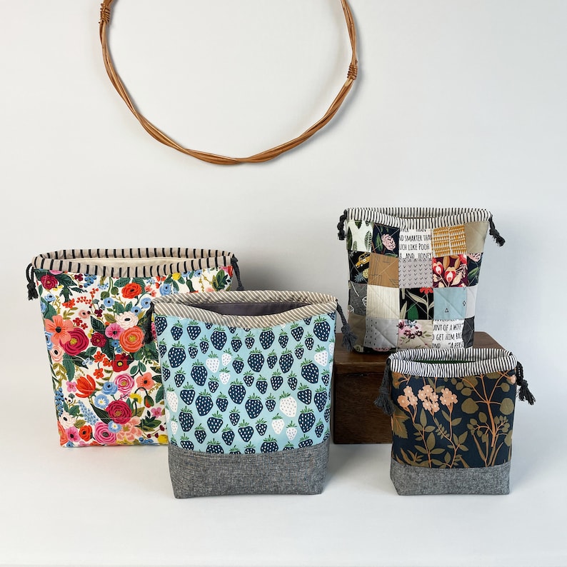 Pode incluir: Quatro sacos de cord&atilde;o com padr&otilde;es diferentes. Os sacos s&atilde;o feitos de tecido e t&ecirc;m um cord&atilde;o cinzento. Os padr&otilde;es incluem flores, morangos, um design de patchwork e um design floral escuro.