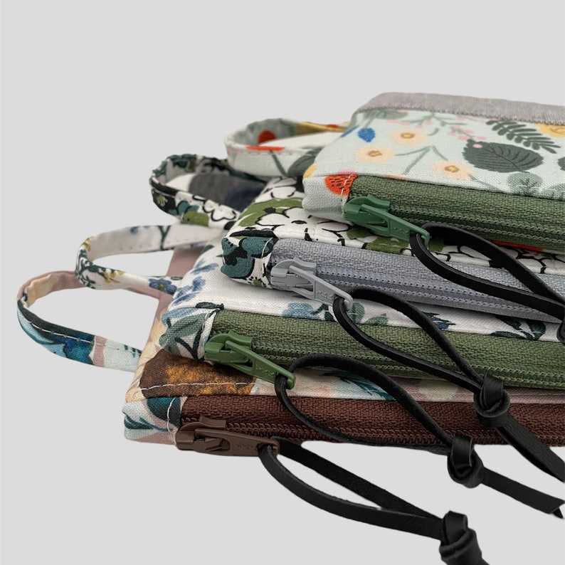 May include: Four fabric pouches with floral patterns and zipper closures. The pouches are stacked on top of each other and have black straps attached to them.