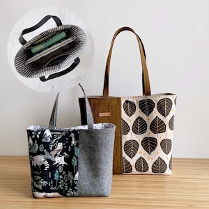 May include: Three tote bags are displayed. One is black with a forest print, another is gray, and the third is brown with a leaf pattern. The bags have handles and are made of fabric. One bag has a striped interior, visible in a circular inset.