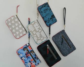Puede incluir: Seis bolsas de cremallera con diferentes patrones y correas de muñeca que cuelgan de una pared. Las bolsas son de varios colores y patrones, incluyendo azul, gris, negro, blanco y floral.