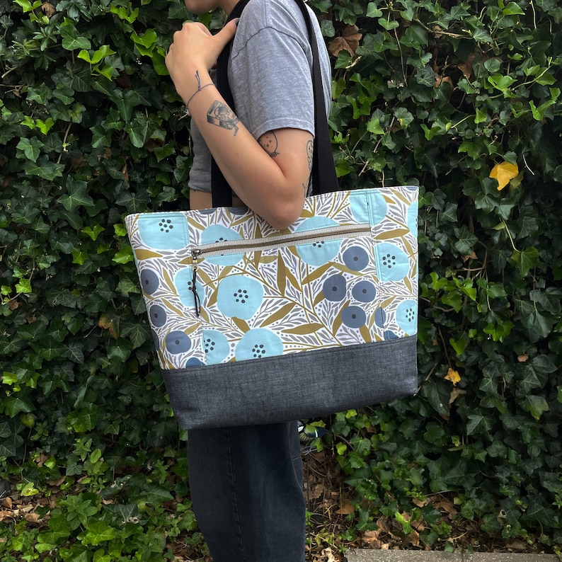 May include: A blue and brown tote bag with a floral pattern. The bag has a zipped pocket and a dark blue base.