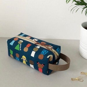 May include: A blue canvas pencil case with a zipper closure and a brown leather handle. The case is decorated with a colorful pattern of geometric shapes and figures.