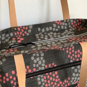 Pode incluir: Uma bolsa tote cinza e rosa com al&ccedil;as de couro e fecho de correr. A bolsa tem um padr&atilde;o geom&eacute;trico com pequenos c&iacute;rculos rosa.