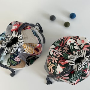 Pode incluir: Duas bolsas de cord&atilde;o de tecido com padr&otilde;es diferentes. Uma bolsa &eacute; feita de tecido patchwork com um design floral e a outra bolsa &eacute; feita de tecido verde escuro com um design floral.