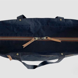 May include: A dark blue canvas tote bag with brown leather handles and a zip closure. The bag is open and the zip is pulled down.