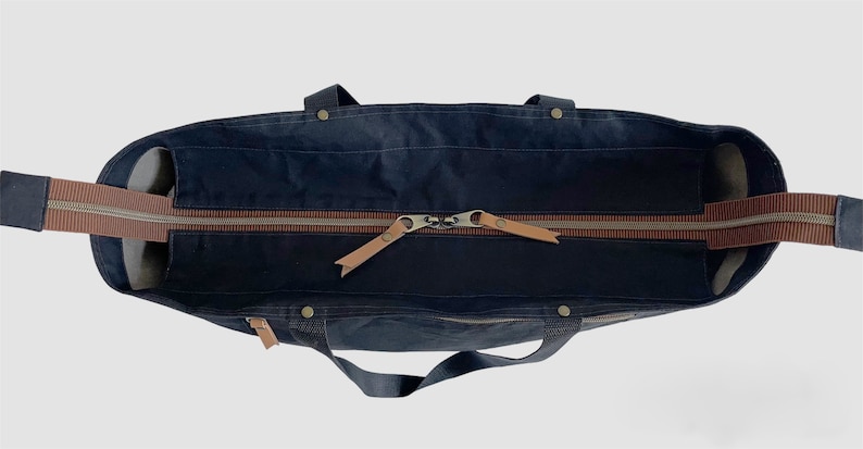May include: A dark blue canvas tote bag with brown leather handles and a zip closure. The bag is open and the zip is pulled down.