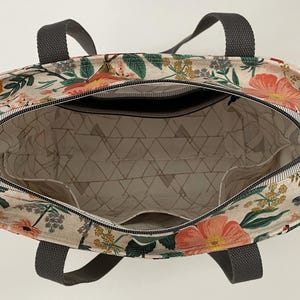 May include: A floral print tote bag with gray handles. The bag is open and the inside is lined with a white fabric with a geometric pattern.