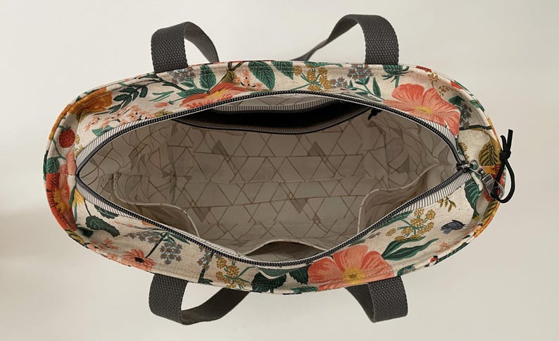 May include: A floral print tote bag with gray handles. The bag is open and the inside is lined with a white fabric with a geometric pattern.