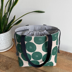 May include: A green and white tote bag with black straps and a drawstring top. The bag has a pattern of large green circles with white dots on a white background.