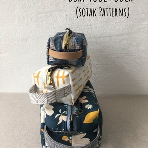May include: Three stacked fabric pouches with zipper closures and handles. The top pouch is blue with a white geometric pattern, the middle pouch is white with a yellow geometric pattern, and the bottom pouch is blue with a floral pattern. The pouches are labeled "Boxy Tool Pouch (Sotak Patterns)".