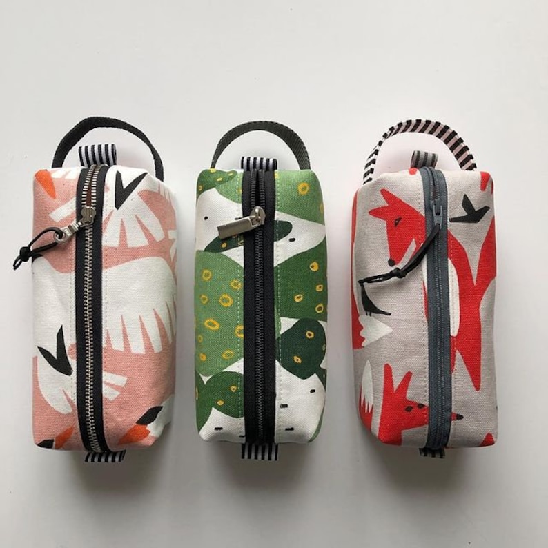 May include: Three zippered pouches with different colorful patterns. The pouch on the left has a pink and white pattern with black accents. The middle pouch has a green and white pattern with black accents. The pouch on the right has a red, white, and gray pattern with black accents.