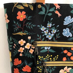 Pode incluir: Sacola tote de lona preta com estampa floral com flores rosa, vermelhas e azuis. A sacola tem dois bolsos com z&iacute;per com z&iacute;peres dourados e puxadores pretos.