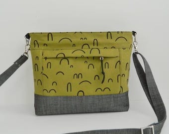 May include: A green crossbody bag with a black and white abstract pattern. The bag has a gray denim bottom and a long adjustable strap.