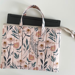 Puede incluir: Una funda acolchada para port&aacute;til de color rosa con un estampado floral que incluye hojas, flores y mariposas. La funda tiene dos asas y una cremallera.