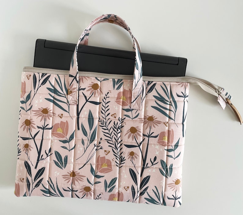 Puede incluir: Una funda acolchada para port&aacute;til de color rosa con un estampado floral que incluye hojas, flores y mariposas. La funda tiene dos asas y una cremallera.