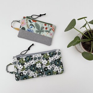 May include: Two zippered pouches with floral patterns. One pouch is green and white with a floral pattern and a gray fabric panel. The other pouch is white with a green and white floral pattern.