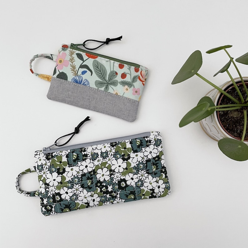 May include: Two zippered pouches with floral patterns. One pouch is green and white with a floral pattern and a gray fabric panel. The other pouch is white with a green and white floral pattern.