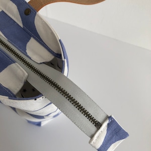 Pode incluir: Uma bolsa tote branca e azul com fecho de correr e al&ccedil;a de couro castanho. A bolsa tem um padr&atilde;o de formas abstratas.