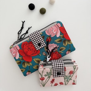 May include: Two floral print zippered pouches. One is teal with red and pink roses, the other is pink with red flowers. Both have black and white checkered accents and black zipper pulls.