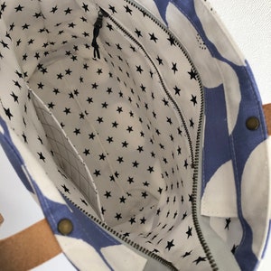 Pode incluir: Uma bolsa tote azul e branca com fecho de correr e forro com padr&atilde;o de estrelas. A bolsa tem duas al&ccedil;as de couro castanho.