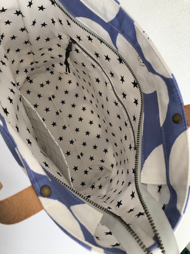Pode incluir: Uma bolsa tote azul e branca com fecho de correr e forro com padr&atilde;o de estrelas. A bolsa tem duas al&ccedil;as de couro castanho.