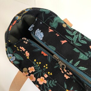 Pode incluir: Uma bolsa tote de lona preta com estampa floral e fecho de z&iacute;per no topo. A bolsa tem uma al&ccedil;a de couro marrom e ferragens de lat&atilde;o.