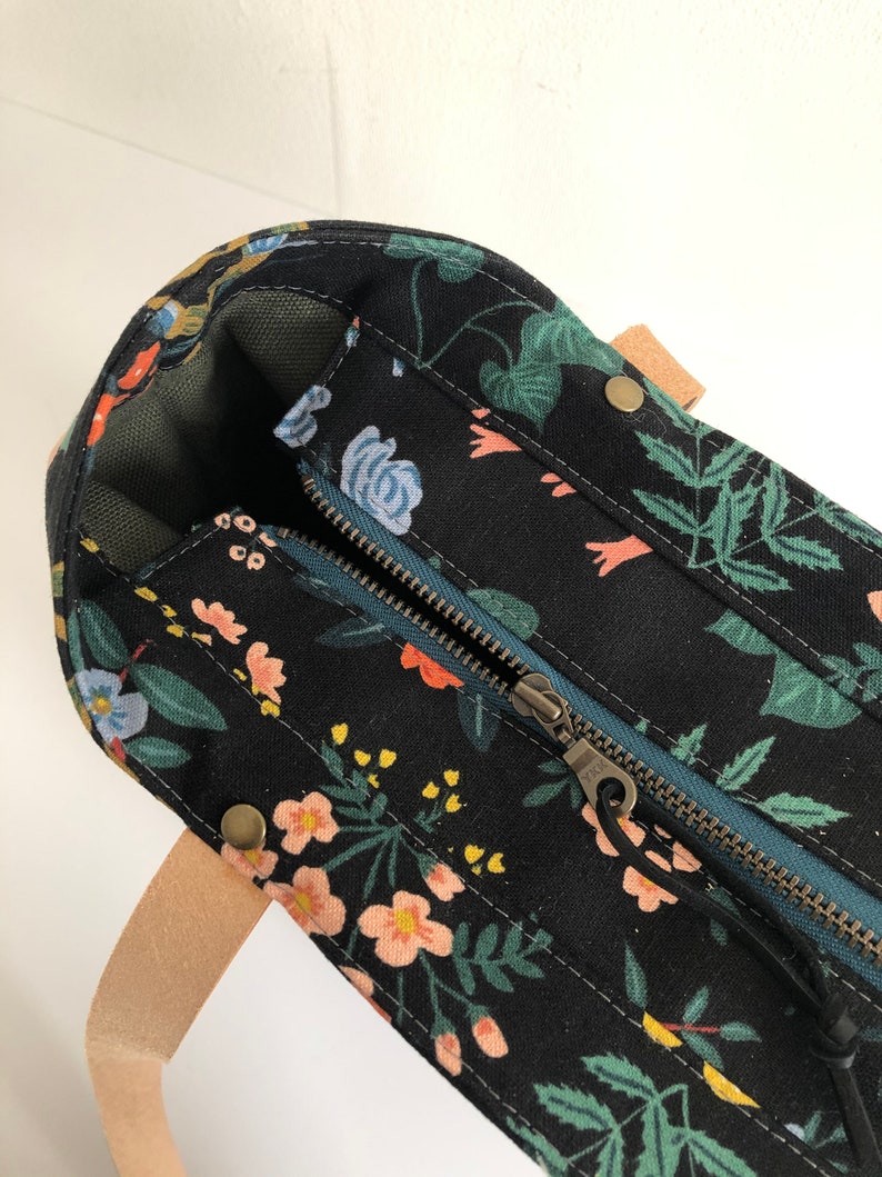 Pode incluir: Uma bolsa tote de lona preta com estampa floral e fecho de z&iacute;per no topo. A bolsa tem uma al&ccedil;a de couro marrom e ferragens de lat&atilde;o.