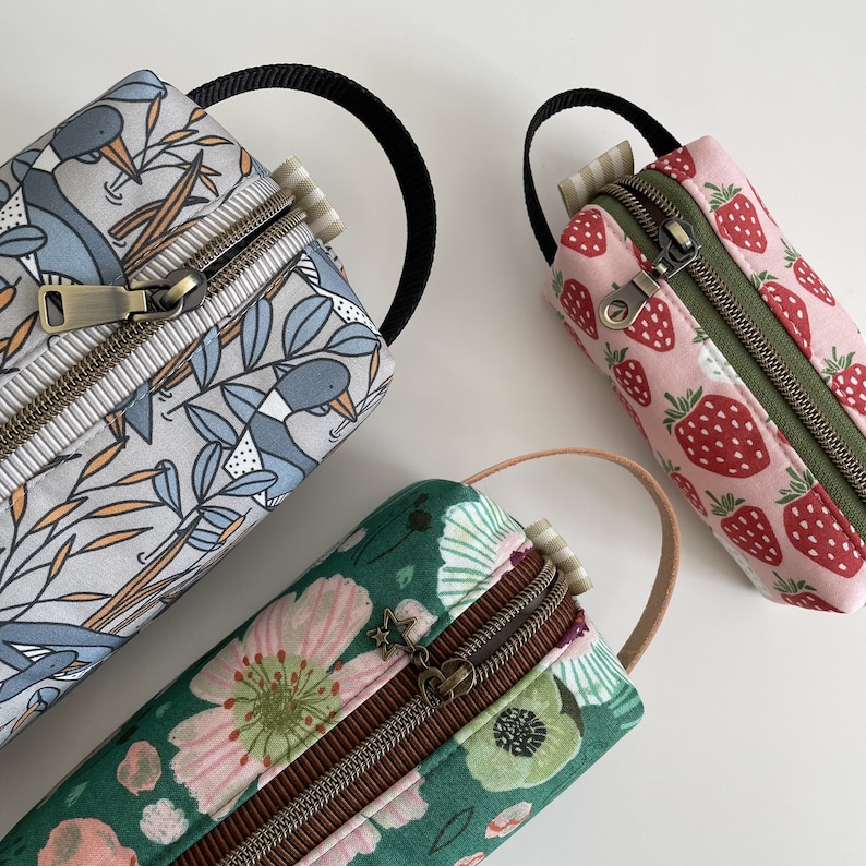 May include: Three zippered pouches with different fabric patterns. The first pouch is gray with a blue and orange bird pattern. The second pouch is green with a pink and green floral pattern. The third pouch is pink with a red strawberry pattern.