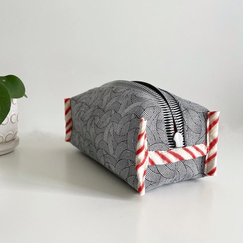 May include: A black and white patterned makeup bag with red and white striped trim. The bag has a zipper closure.