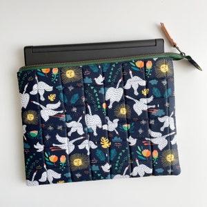 Puede incluir: Una funda para port&aacute;til de color azul oscuro con un dise&ntilde;o acolchado que presenta cisnes blancos y patrones florales coloridos. La funda tiene una cremallera y una leng&uuml;eta de cuero marr&oacute;n.