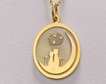 May include: Gold necklace with a pendant featuring two cats sitting on a crescent moon with stars. The pendant is oval shaped and has a detailed design.