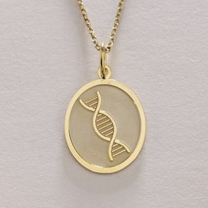 Puede incluir: Un collar de cadena de oro con un colgante redondo que presenta un diseño de doble hélice de ADN grabado en detalle.
