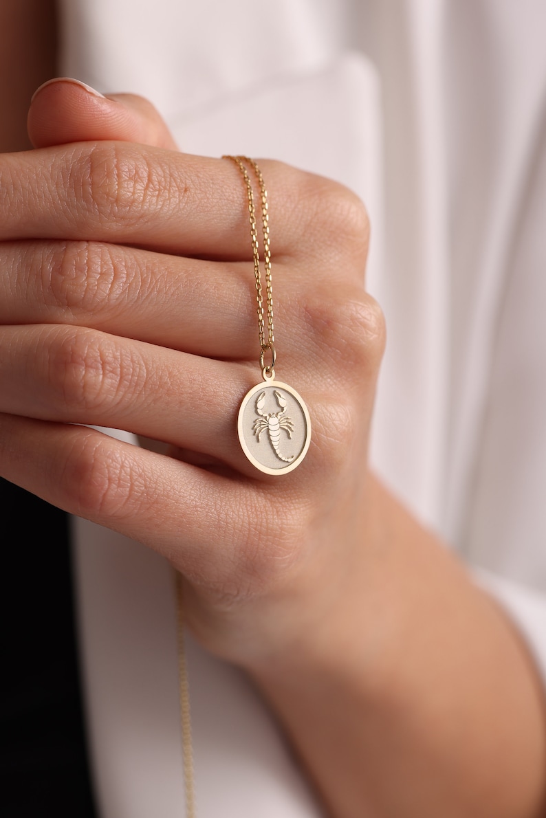 May include: A gold chain necklace with a round pendant featuring a detailed scorpion design.