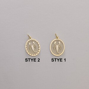 May include: Two gold-toned pendants featuring a scorpion design. The pendant on the left has a more intricate border, while the pendant on the right has a simpler border. The text "STYE 2" is below the left pendant, and the text "STYE 1" is below the right pendant.