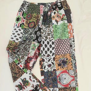 May include: Patchwork trousers in a vibrant mix of patterns and colours. The design incorporates floral, geometric, and paisley motifs in red, green, black, white, and brown. The trousers have a drawstring waist and a relaxed fit.